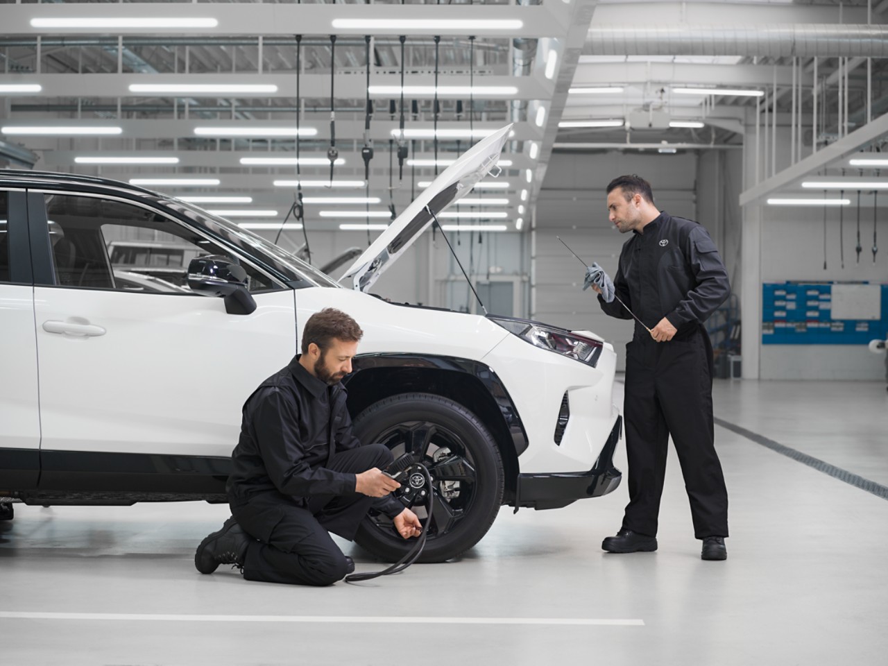 Två tekniker inspekterar en Toyota RAV4 i en verkstadslokal.